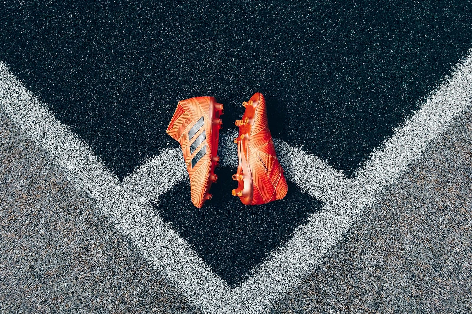 Pair of orange football boots laid on a corner marking of the pitch