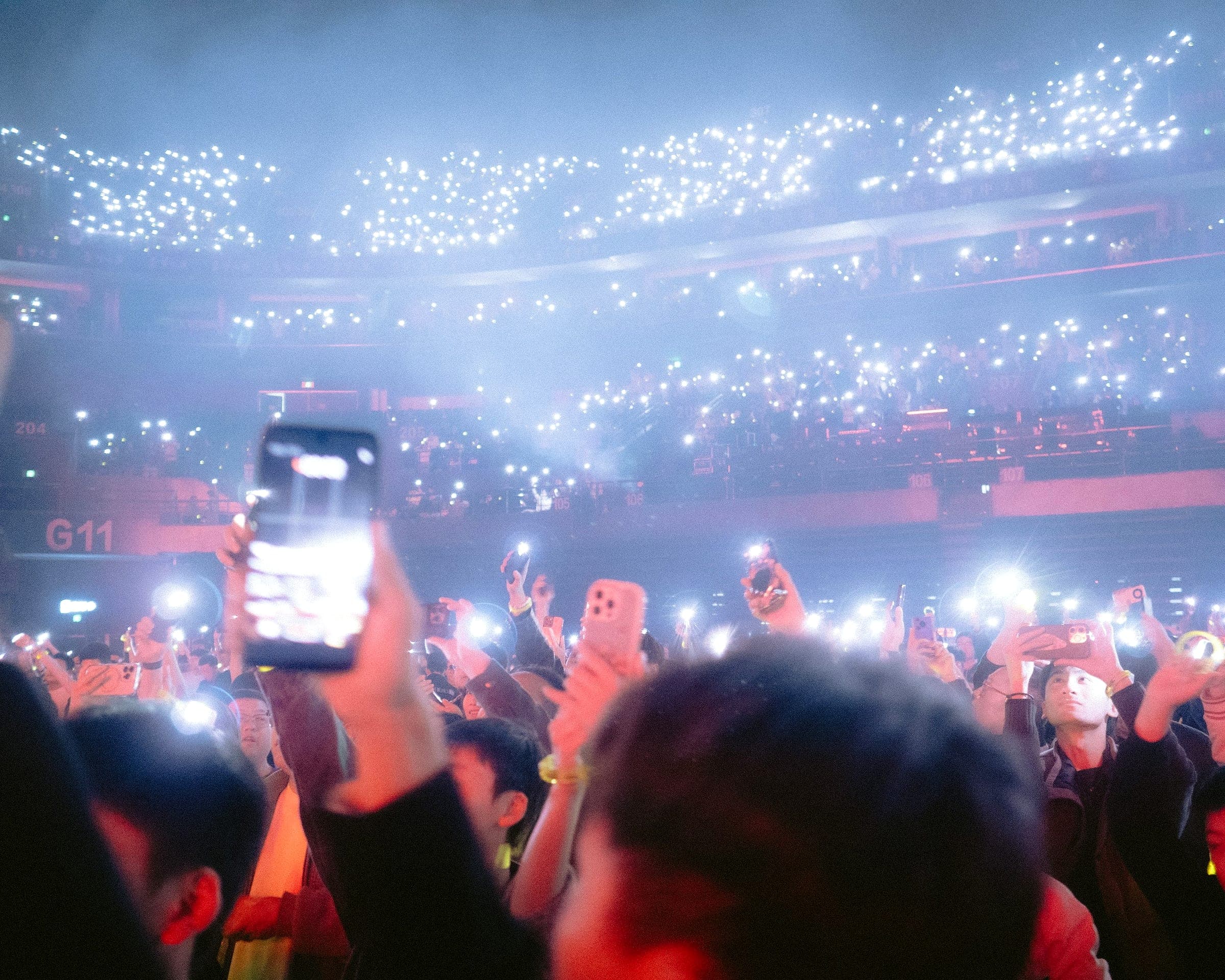 Crowd holding up phones with flashlights glowing across a packed arena