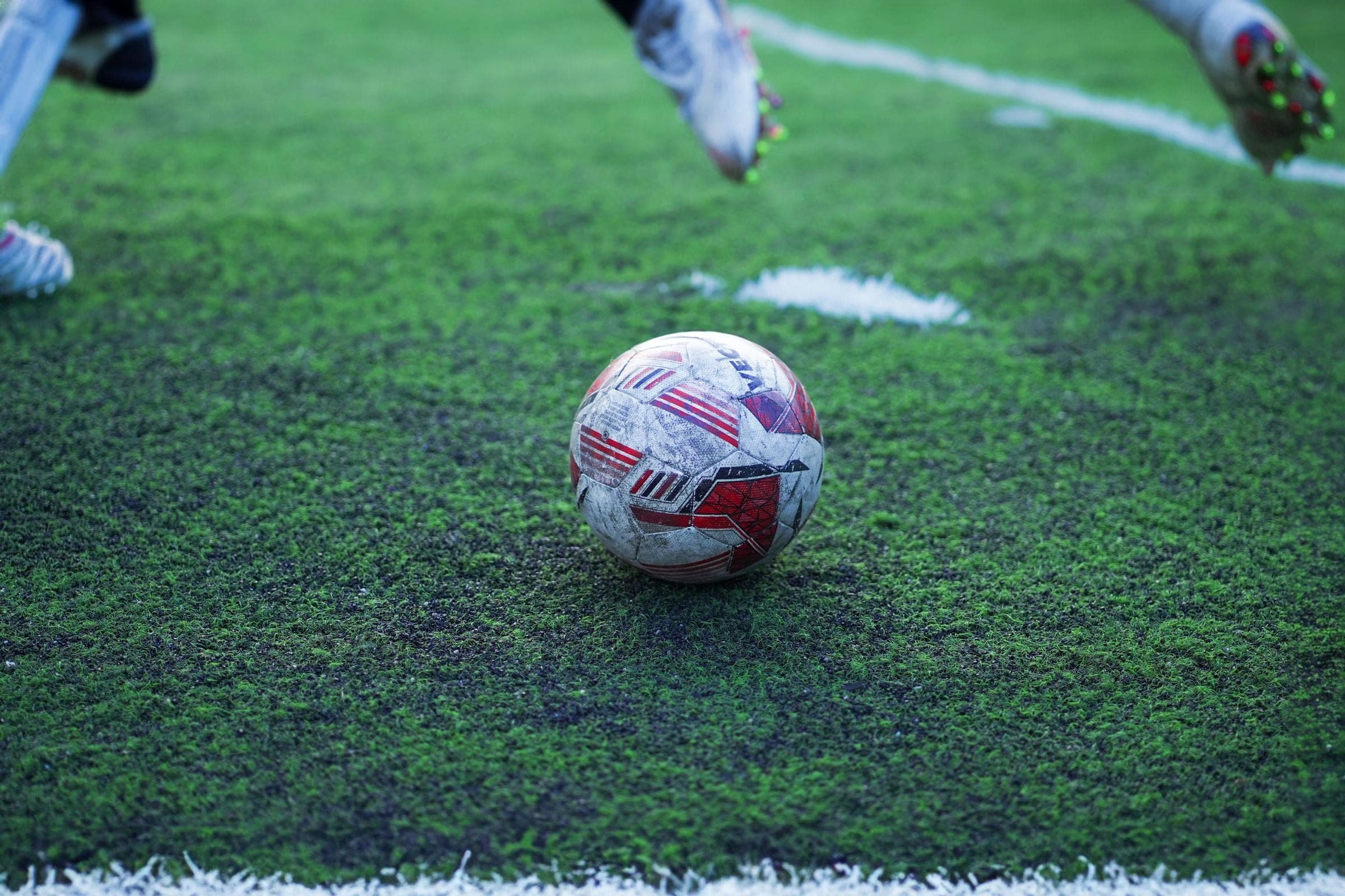 Football on the turf between a player's boots, pitch markings behind